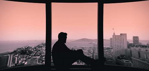person silhouette of person sitting on building's window window
