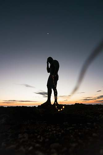 human silhouette of person standing on rock during sunset person