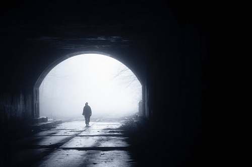 tunnel silhouette of person walking out from tunnel during daytime alone