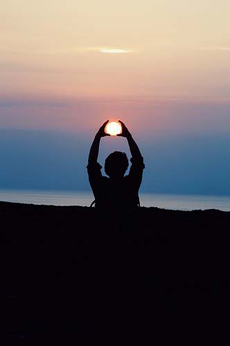yoga silhouette of person with both hands over his head tracing the sun during golden hour photography sun