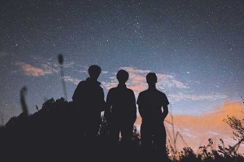 person silhouette of three people standing on tall grass during nighttime human