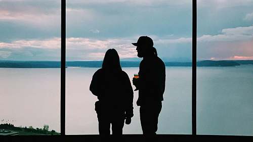 human silhouette of two person standing near body of water person