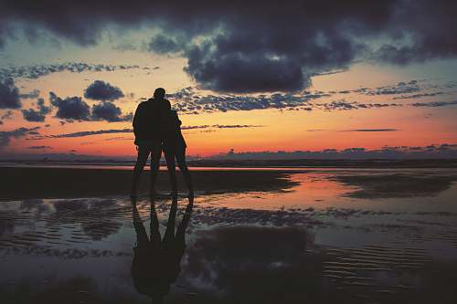 person silhouette of two person standing near seashore outdoors