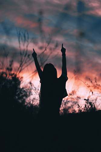 light silhouette of woman raising hands facing sun during golden hour flare