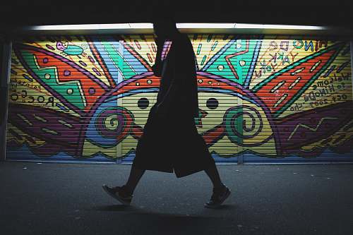 wall silhouette photo of a man wearing shorts standing near painted roller shutter art