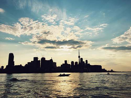 boat silhouette photo of buildings beside sea nature