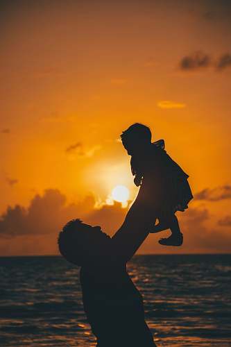 sunlight silhouette photo of man carrying baby during golden hour light