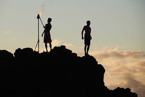 human silhouette photo of man holding fire stick near man standing at peak of mountain person