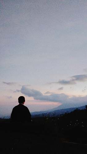 human silhouette photo of man sitting on rock formation grey