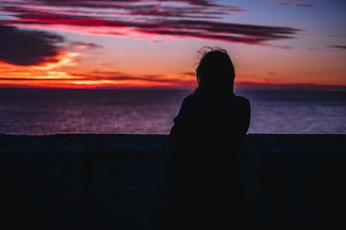 sunset silhouette photo of person standing while looking at the ocean during golden hour sunrise