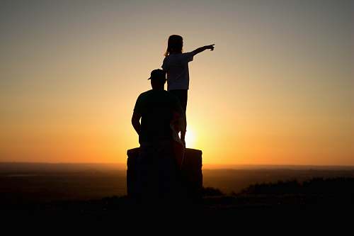 human silhouette photo of two person sitting on cliff people