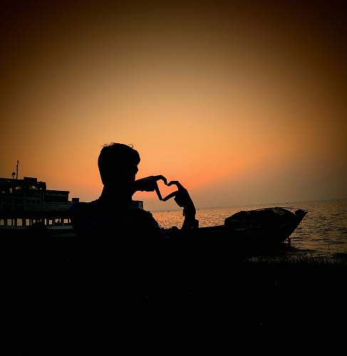 human silhouette photography of man making heart hand sign person