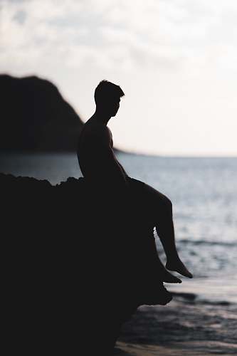 human silhouette photography of man siting on a cliff nature
