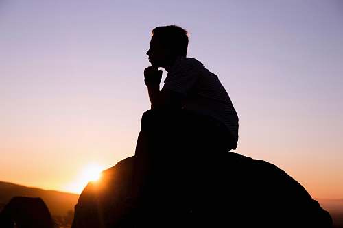 person silhouette photography of man sitting on stone human