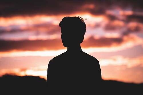 black silhouette photography of man standing in front of red sky 