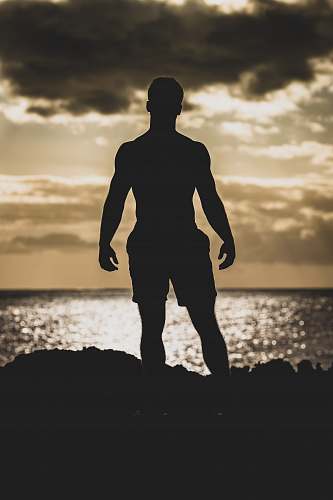 nature silhouette photography of man standing on rock formation near body of water outdoors