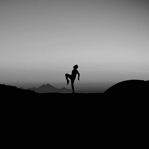 black-and-white silhouette photography of man standing with one leg on ground grey