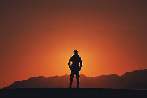 person silhouette photography of person standing on platform with mountain background during golden hour people