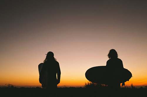 human two person walking on road while holding surfboard during golden hour person