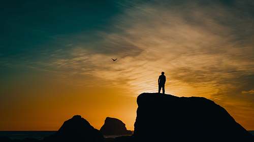 silhouette silhouette of man on cliff under blue sky during golden hour sky