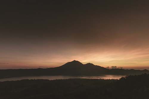 sunrise silhouette of mountain near body of water under brown clouds lake
