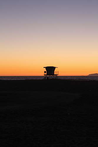 sunrise silhouette photo of shed on sand near sea during golden hours dawn