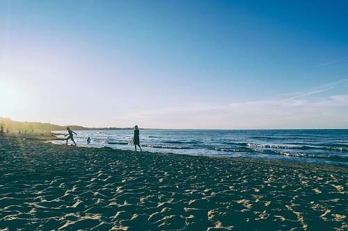coast two person walking on seashore during daytime ocean