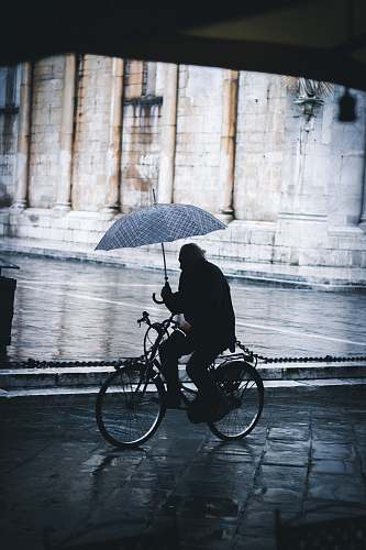 bike man riding bicycle while holding umbrella near street cyclist