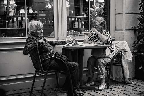 woman grayscale photo of two woman sitting beside the table women