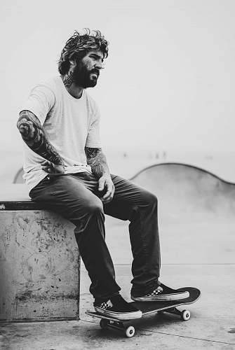 human grayscale photography of man sitting on bench while his feet on skateboard people