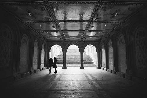 building grayscale two people standing on hallway arch