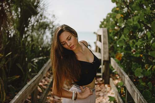 female woman standing on bridge in between trees during daytime woman