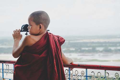 people boy in red apparel leaning on blue and red metal railing during daytime person
