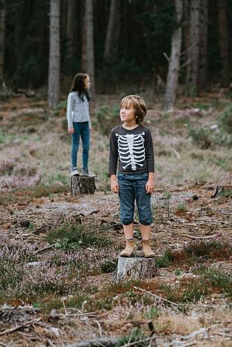 people boy standing on chopped log in middle of forest during daytime person