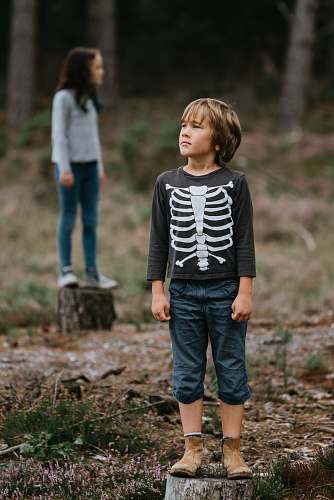 people boy wearing black and white skeleton-printed crew-neck sweatshirt while standing on log person