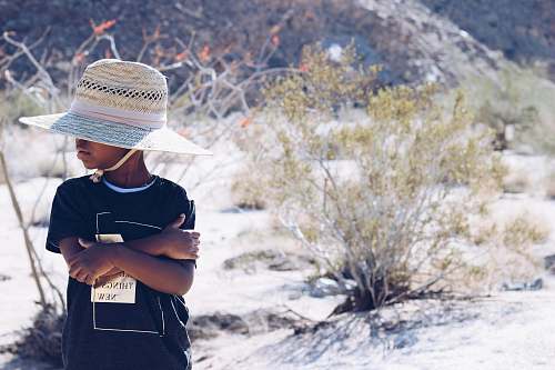 people boy wearing black shirt and white hat standing beside green leafed plant person