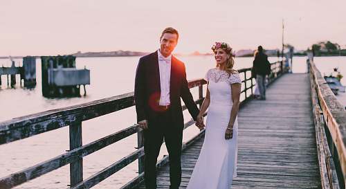 people bride and groom standing on wooden dock near body of water person