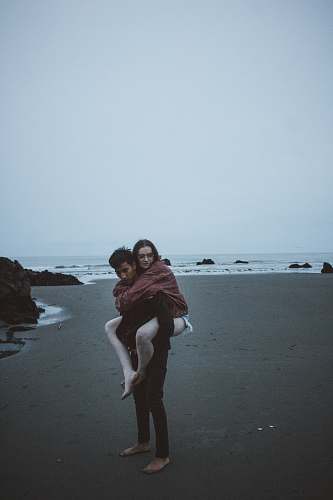 people candid photography of man carrying woman at back near seashore person