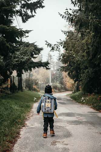 people child carrying backpack while standing near green trees and plants person