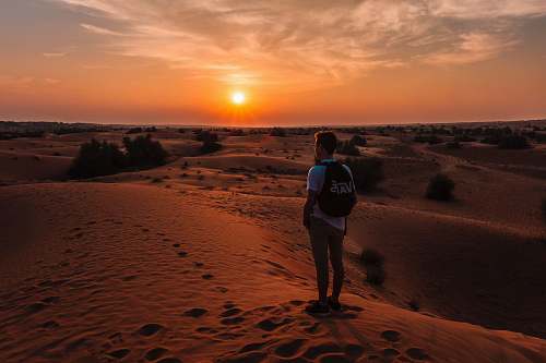 person golden hour photography of man standing on top of a hill people
