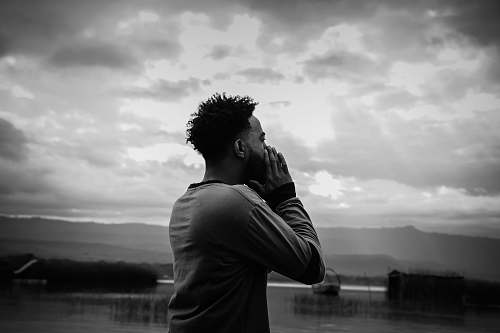 people grayscale photo of man standing holding his face black-and-white