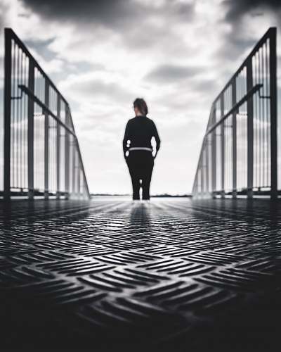 person grayscale photo of woman in between gray metal railings black-and-white