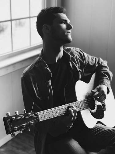 person grayscale photography of man playing acoustic guitar black-and-white