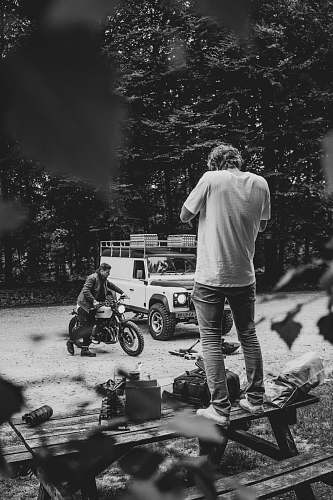 person grayscale photography of man standing on picnic table black-and-white
