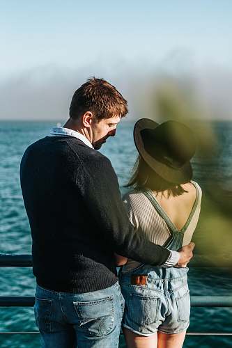 person man and woman standing beside metal rail near body of water people