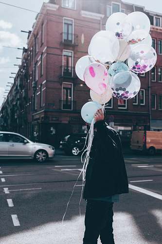 person man holding white balloon walking on street during day time people