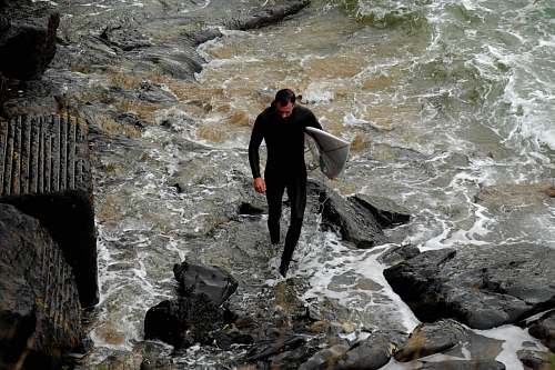 people man holding white surfboard while walking on rocks person