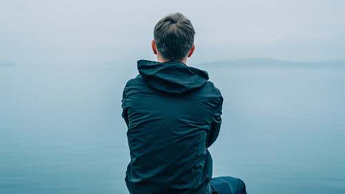 people man in black hoodie sitting in front of ocean person