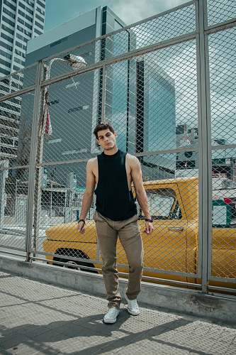 person man in black tank top and brown jeans standing beside of wire fence during daytime people