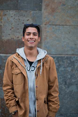 people man in brown coat standing near concrete wall smiles person